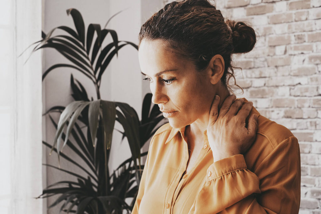 A woman wearing a yellow blouse holding her neck & looking down. Representing how childhood trauma can affect you in your adult life. Get started with trauma therapy in Katy, TX today.