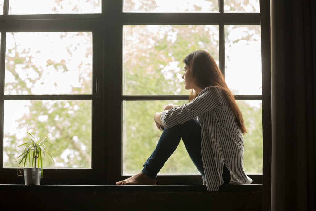 A woman sitting alone in a large windowsill. If you struggle with anxiety, you don't have to navigate it alone. Get started with an anxiety therapist in Katy, TX today.