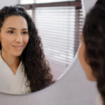 A woman with brown curly hair smiling gently in the mirror. Finding a therapist in Katy, TX is important for your tailored healing journey. Reach out today for counseling.