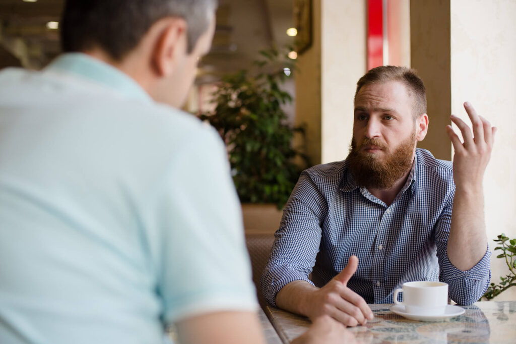 A professional looking man talking to a friend with his hands in a cafe. Therapy in Katy is here to support you with parenting challenges & behavioral issues. Reach out today for support. 