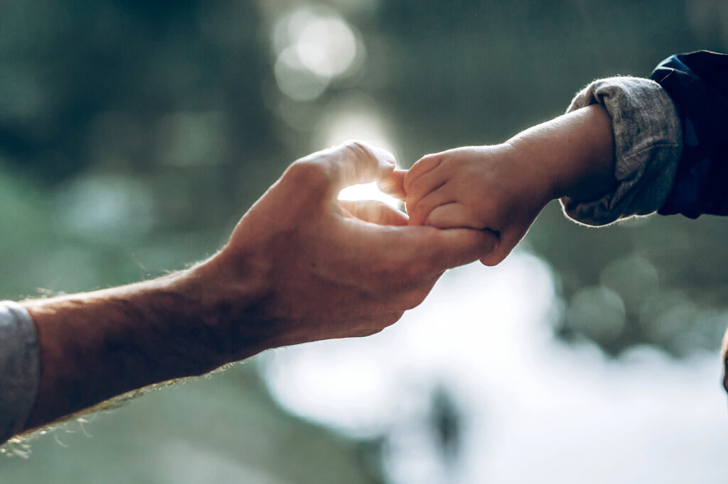 A parents hand holding a young child's hand with sunlight in the background. Curious to learn more about your attachment style? Take our quiz here & begin working with an adult therapist in Katy, TX.