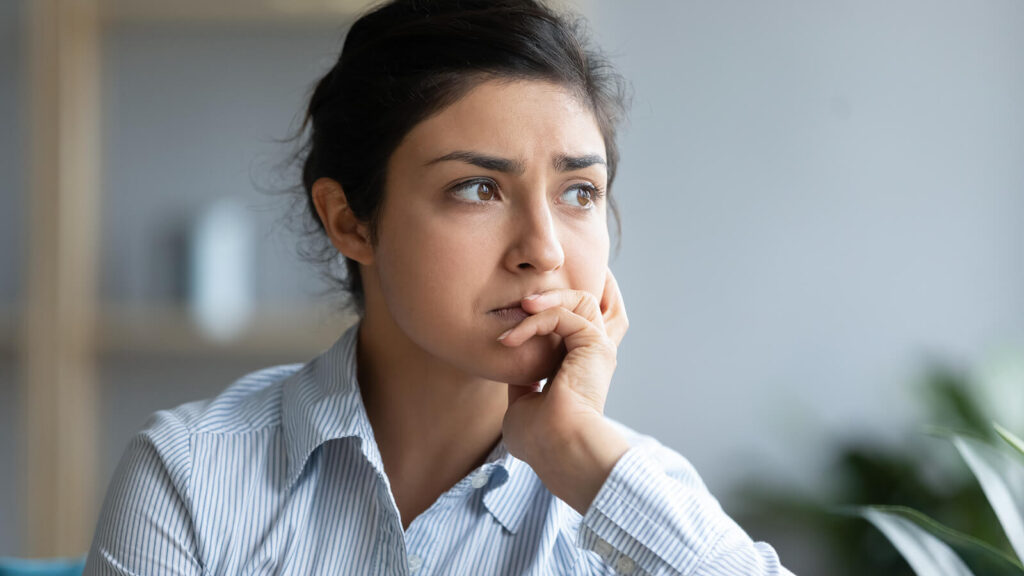 A woman looking anxiously while holding her chin. Trauma therapy in Katy, TX can help with complex PTSD, chronic shame & regulating emotions. Learn more here!